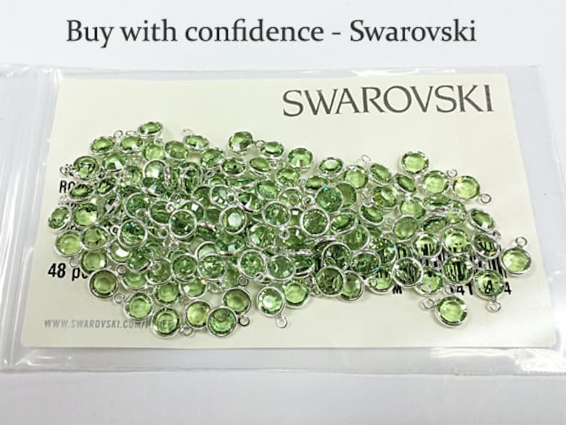 Puede incluir: Primer plano de un paquete de 48 cuentas de cristal verde con lazos plateados. El paquete est&aacute; etiquetado con "SWAROVSKI" y "48 pc".