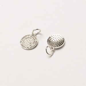 May include: Two silver charms, one with a round, textured surface and the other with a round surface covered in small, clear stones.