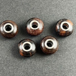 May include: Five dark brown wooden beads with silver metal accents. Each bead has a hole in the center for stringing.