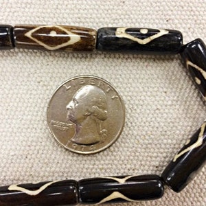 May include: A close-up of a string of black and white cylindrical beads with a geometric pattern. The beads are about the size of a US quarter.