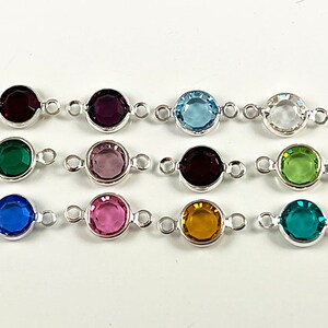Puede incluir: Doce abalorios conectores de plata con piedras preciosas redondas y facetadas en varios colores, incluyendo rojo, morado, azul, verde, rosa, amarillo y transparente.