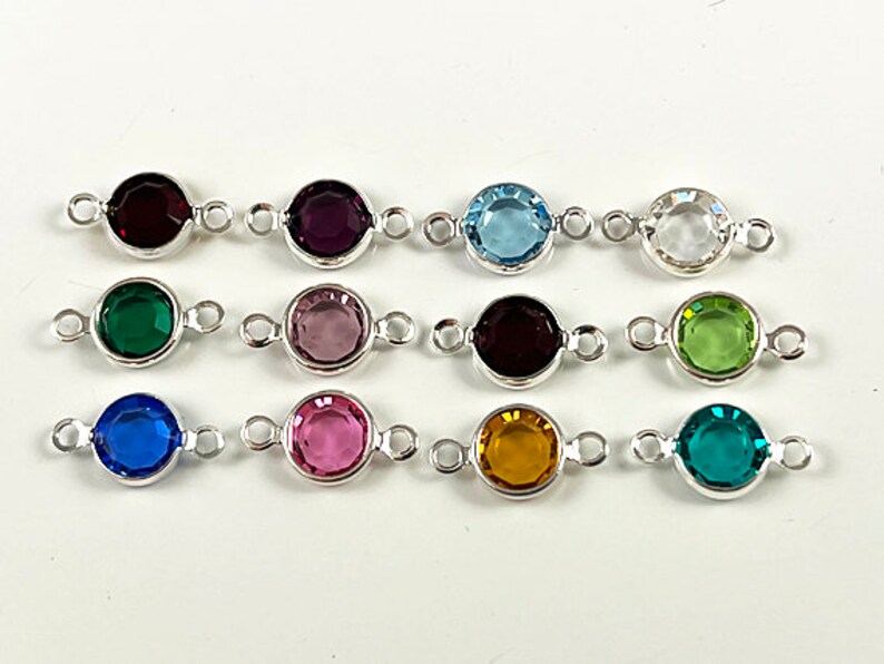 Puede incluir: Doce abalorios conectores de plata con piedras preciosas redondas y facetadas en varios colores, incluyendo rojo, morado, azul, verde, rosa, amarillo y transparente.