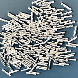 Könnte beinhalten: Ein großer Haufen silberner Metallperlen, jede Perle ist ein kleiner Zylinder mit einer strukturierten Oberfläche.