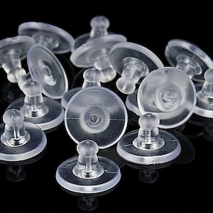 May include: A group of clear plastic earring backs. The backs are designed to be used with post earrings. They have a small, round base and a raised center post.