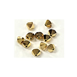 May include: A group of gold-colored glass beads with a pointed, conical shape. The beads are scattered on a white surface.