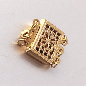 May include: Gold-toned metal clasp with a decorative, openwork design. The clasp has three loops for attaching to a necklace or bracelet.