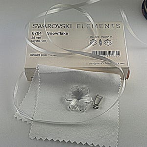 Swarovski Magic Classic Crystal snowflake ornament .A silver snowflake pendant necklace with a clear crystal snowflake charm. The necklace has a white satin ribbon.