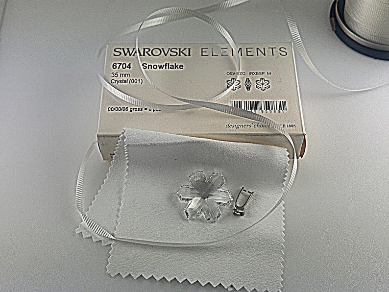 Swarovski Magic Classic Crystal snowflake ornament .A silver snowflake pendant necklace with a clear crystal snowflake charm. The necklace has a white satin ribbon.