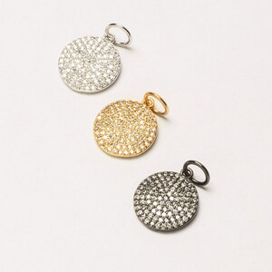 May include: Three round pendants with a pave setting of clear stones. The pendants are silver, gold, and black.