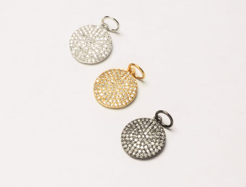 May include: Three round pendants with a pave setting of clear stones. The pendants are silver, gold, and black.