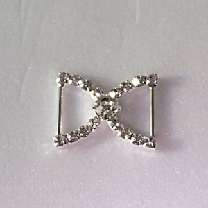 May include: Silver-toned metal buckle with a clear rhinestone design. The buckle has a center stone and is shaped like a bow.
