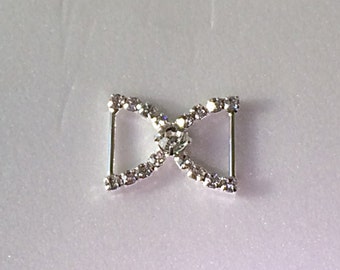 May include: Silver-toned metal buckle with a clear rhinestone design. The buckle has a center stone and is shaped like a bow.
