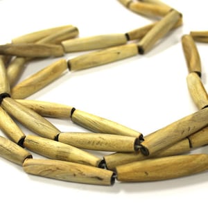 May include: A close-up of a long necklace made of natural wood beads. The beads are a light brown color and have a smooth, polished finish. The necklace is strung on a thick cord and has a simple design.