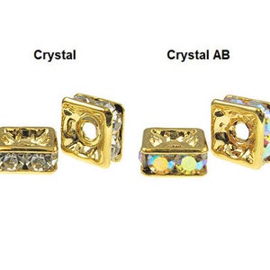 May include: Two gold-toned square bead caps with a hole in the center. The bead caps are adorned with clear crystals. The left bead cap is labeled "Crystal" and the right bead cap is labeled "Crystal AB".