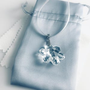 Swarovski Magic Classic Crystal snowflake ornament .A silver snowflake pendant necklace with a clear crystal snowflake charm. The necklace has a white satin ribbon.