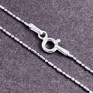 May include: A silver chain necklace with a lobster clasp closure. The chain is made of small, round links.