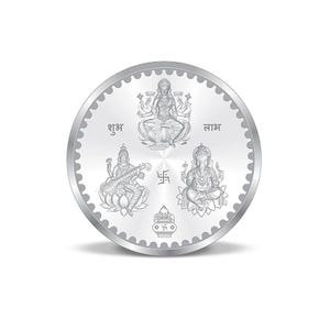 May include: A round, silver coin featuring detailed engravings of Hindu deities. The coin has a scalloped edge and includes the words "शुभ" and "लाभ". The coin depicts Lakshmi, Saraswati, and Ganesha, symbols of prosperity and wisdom.