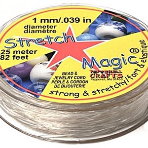 May include: A spool of clear elastic stretch magic cord for beading and jewellery making. The spool is labelled "Stretch Magic" with a red star and the text "1 mm/.039 in diameter, 25 metre, 82 feet, Bead & Jewellery Cord, Perle & Cordon de Bijouterie, strong & stretchy/fort & elastique".