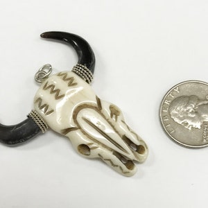 Peut inclure: Pendentif en os de cr&acirc;ne de taureau blanc avec des cornes noires et des accents de fil argent&eacute;. Le pendentif est &agrave; peu pr&egrave;s de la taille d'une pi&egrave;ce de 25 cents am&eacute;ricaine.