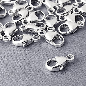 May include: A pile of silver-toned lobster claw clasps, a type of jewelry finding used for attaching chains or cords to jewelry pieces.