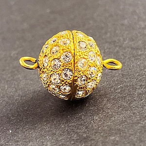 Op de afbeelding: Gouden magnetische sluiting met heldere strass steentjes. De sluiting is rond en heeft aan beide zijden twee lussen.