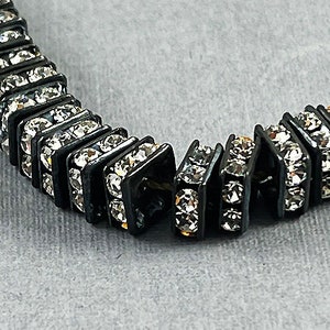 May include: A black and silver bracelet with a repeating pattern of square-shaped rhinestones.