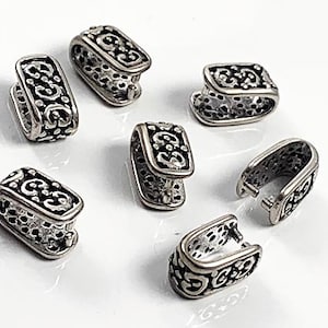 May include: Seven silver-toned metal clasps with an ornate design. Each clasp has a rectangular shape with a decorative pattern.
