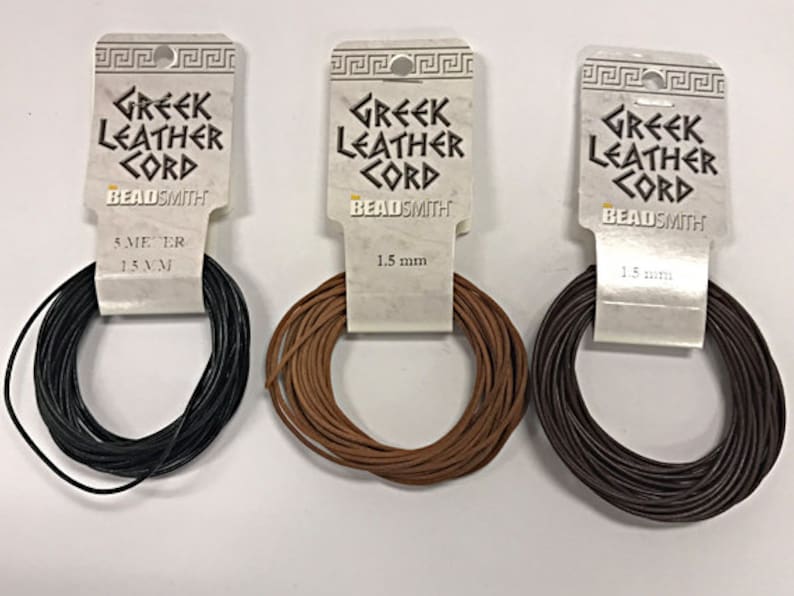 K&ouml;nnte beinhalten: Drei Spulen mit 1,5 mm griechischem Lederband in Schwarz, Braun und Beige. Jede Spule ist mit "Griechisches Lederband" und "Beadsmith" beschriftet.