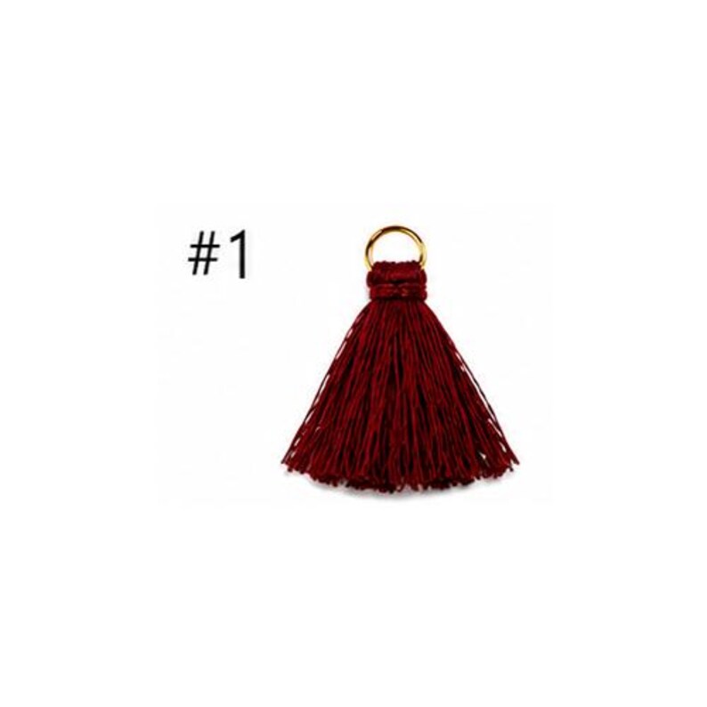 Peut inclure: Un pompon rouge fonc&eacute; dot&eacute; d'un anneau m&eacute;tallique dor&eacute; sur le dessus pour la fixation. Le pompon est compos&eacute; de nombreux fils fins et pendants qui s'&eacute;vasent &agrave; partir du centre. Le texte #1 est visible &agrave; gauche du pompon.