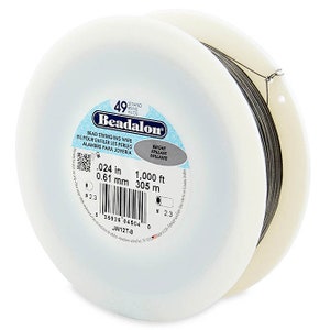 Op de afbeelding: Een spoel Beadalon 49-strengs kralen draad. De draad is 0,61 mm dik en 305 meter lang. De spoel is van wit plastic met een label met de tekst "Beadalon" en een barcode.