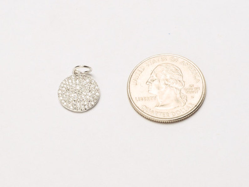 May include: A silver charm with a round, pave-set diamond design. The charm is approximately the size of a US quarter.