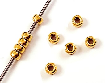 May include: A close-up of gold-colored metal beads strung on a silver wire. The beads are round and have a smooth, polished finish. There are seven beads in total, with six of them on the wire and one off to the side.