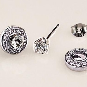 May include: A pair of silver earrings with a round, clear crystal center surrounded by smaller crystals. The earrings have a post back.