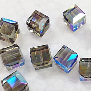 May include: Ten iridescent, faceted, square-shaped glass beads. The beads are a dark gray color with a blue and green iridescent sheen.