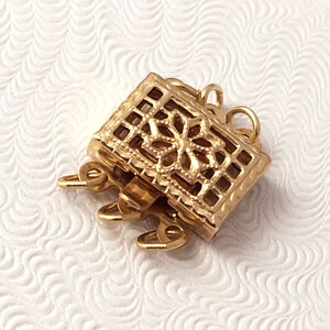 May include: Gold-toned metal clasp with a decorative filigree design. The clasp has multiple loops for attaching jewelry.