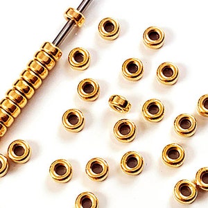 K&ouml;nnte beinhalten: Nahaufnahme einer Ansammlung von goldfarbenen Metallperlen. Die Perlen sind rund und haben eine glatte Oberfl&auml;che. Sie sind in einem zuf&auml;lligen Muster auf einer wei&szlig;en Oberfl&auml;che angeordnet.