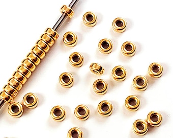 May include: A close-up of a pile of gold-colored metal beads. The beads are round and have a smooth finish. They are arranged in a random pattern on a white surface.