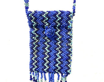May include: A small, beaded bag in shades of blue, white, and gray. The bag features a chevron pattern and a button closure. The strap and the bottom of the bag have beaded fringe.