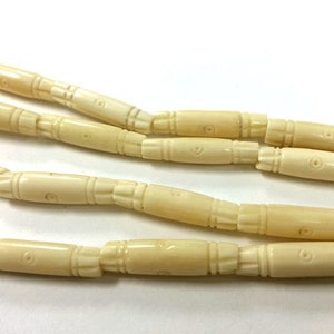 May include: A strand of off-white carved bone beads. The beads are cylindrical and have a decorative pattern carved into them.