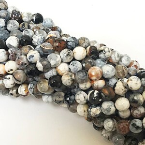 May include: A strand of round, white agate beads with brown and black markings. The beads are approximately 8mm in diameter and have a natural, polished finish.
