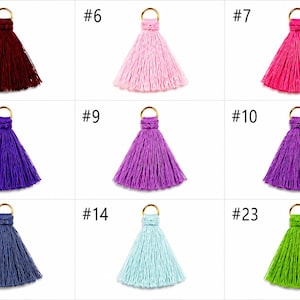 Peut inclure: Un ensemble de neuf pompons d&eacute;coratifs en tissu de diff&eacute;rentes couleurs, chacun dot&eacute; d'un anneau m&eacute;tallique dor&eacute; au sommet. Les couleurs incluent le rouge fonc&eacute;, le rose clair, le rose vif, le bleu roi, la lavande, le violet, le bleu marine, le bleu clair et le vert lime.