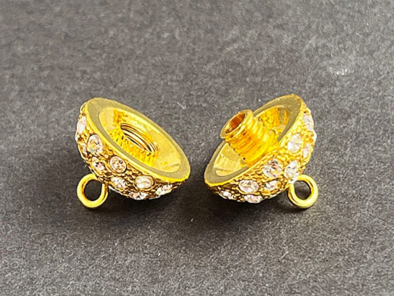 Op de afbeelding: Twee gouden metalen kralencaps met heldere strasssteentjes. Elke dop heeft een lus aan de zijkant en een schroefgat aan de bovenkant.