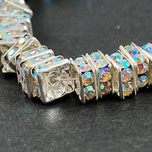May include: A silver bracelet with iridescent square-shaped crystals. The bracelet is made of metal and has a clasp closure.