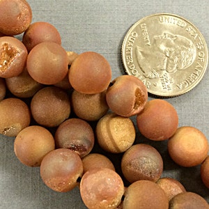 May include: A strand of brown agate beads with a frosted finish. The beads are round and have a natural, earthy look. The beads are approximately the size of a US quarter.