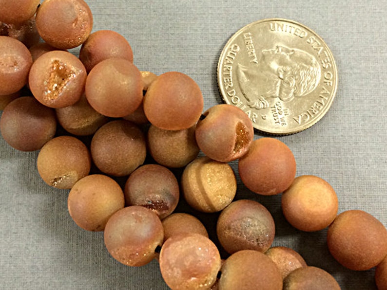 May include: A strand of brown agate beads with a frosted finish. The beads are round and have a natural, earthy look. The beads are approximately the size of a US quarter.