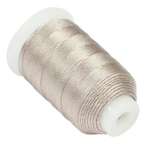 May include: A spool of metallic, light taupe-colored thread. The thread is tightly wound around a white plastic spool. The thread has a slight sheen, reflecting light. The spool is angled slightly, showing the thread's texture and color.