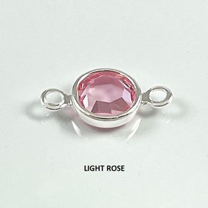 Puede incluir: Un conector plateado con un cristal de color rosa claro en el centro. El conector tiene dos bucles a cada lado.