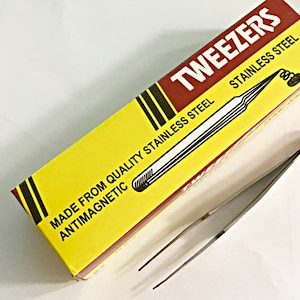 May include: A yellow and red package with the text "TWEezers STAINLESS STEEL" and "MADE FROM QUALITY STAINLESS STEEL ANTIMAGNETIC" on it. The package contains a pair of silver tweezers.
