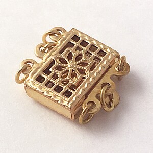 May include: Gold-toned metal clasp with a decorative filigree design. The clasp has three loops for attaching jewelry.