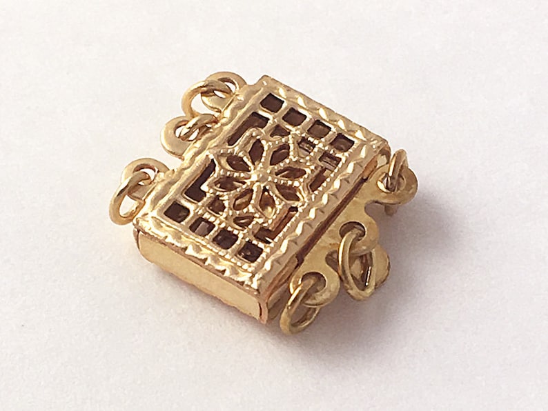 May include: Gold-toned metal clasp with a decorative filigree design. The clasp has three loops for attaching jewelry.